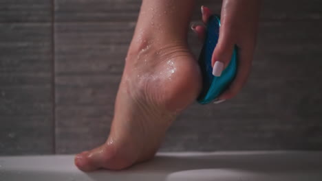 woman rubs heel with foot file in bathroom closeup. elegant lady peels dry skin from sole leaning on bathtub edge. feet care procedure supply