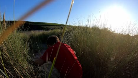 vista trasera de un niño en vacaciones en la playa corriendo a través de dunas de arena contra el sol abrasador