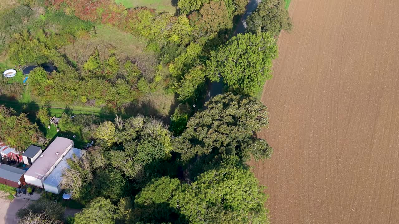 Aerial drone flyover of Nasty, Hertfordshire, England. The camera follows the road out of the hamlet, showing green and brown fields, trees, with the drone gliding past the road’s sharp turn