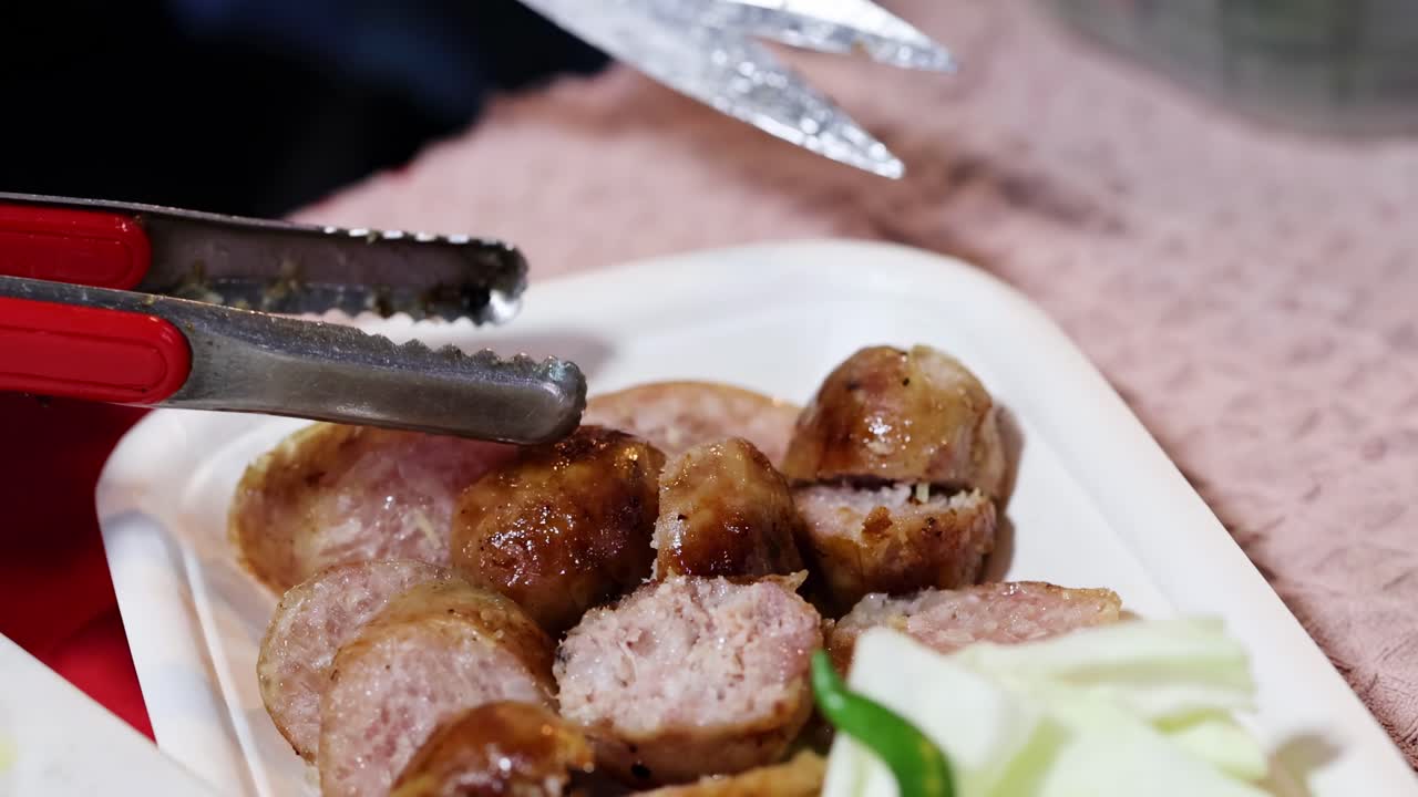 A detailed view of sausages being arranged with cucumber slices on a plate using tongs.