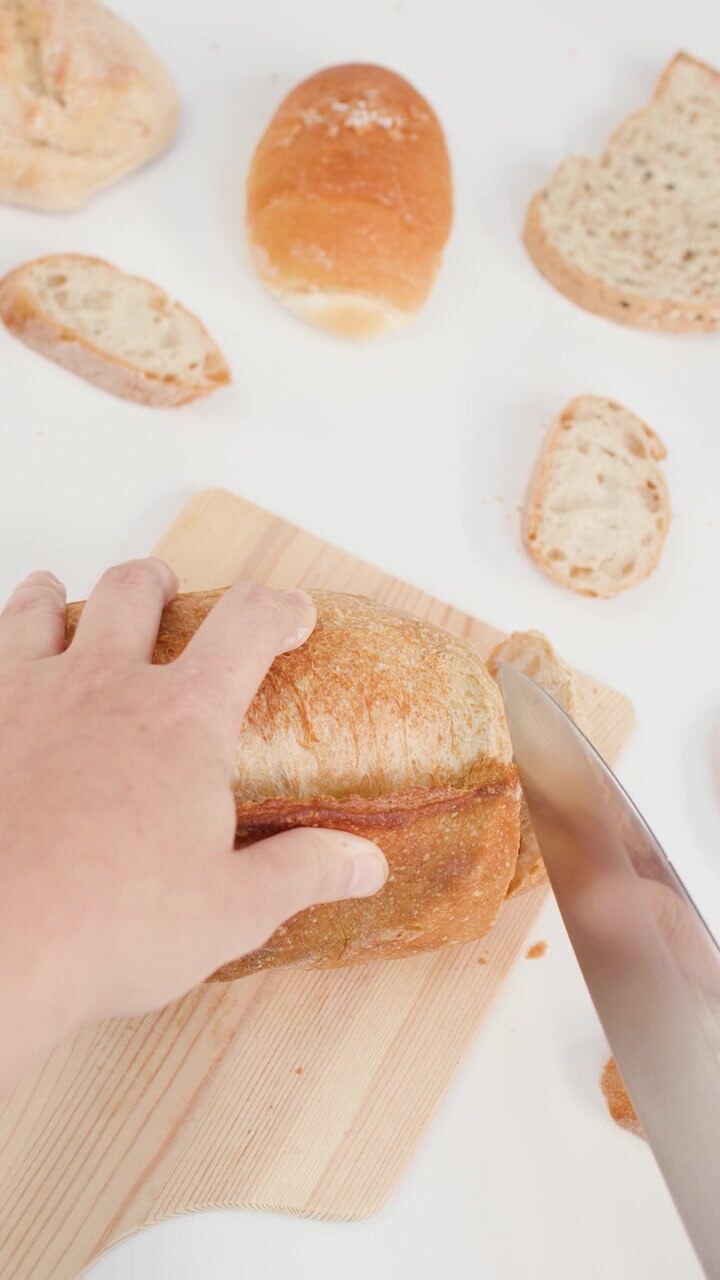 Overhead shot of hands using a knife to slice crusty bread on a white background.