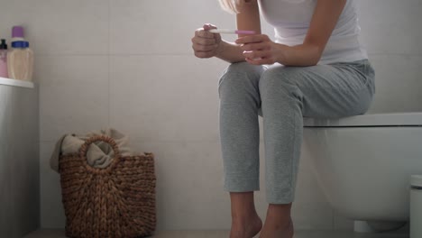 stressed unrecognizable woman sitting on toilet and waiting for pregnancy test results.