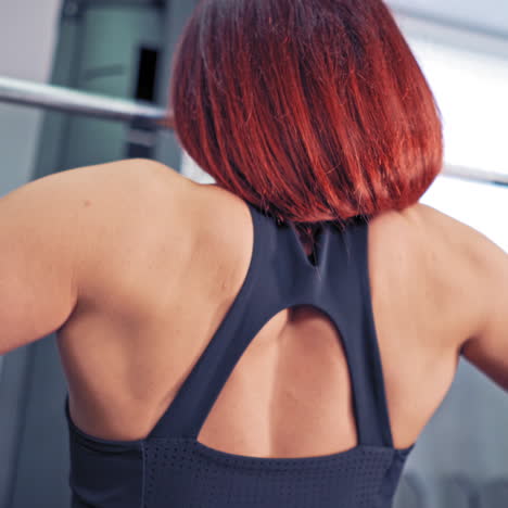 close-up of female's back working on simulator indoors. athletic woman is doing exercise while pulling the metal bar down at the fitness centre. personal trainer man and a sportswoman.