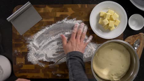 overhead shot of kneading bread dough and dividing bread dough in half on a floured wood cutting board surface