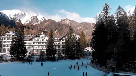 slow motion aerial pan of people walking on the frozen lake braies near a large hotel with the italian dolomites in the background