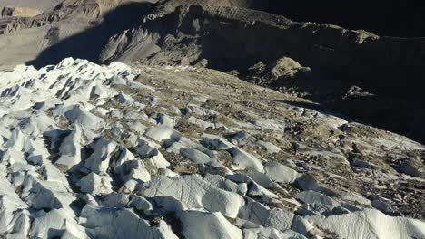 drone aéreo volando sobre las grietas del glaciar passu en hunza pakistán junto con tierra y roca mezclada con la nieve blanca entre las montañas de conos passu durante la puesta de sol en el verano