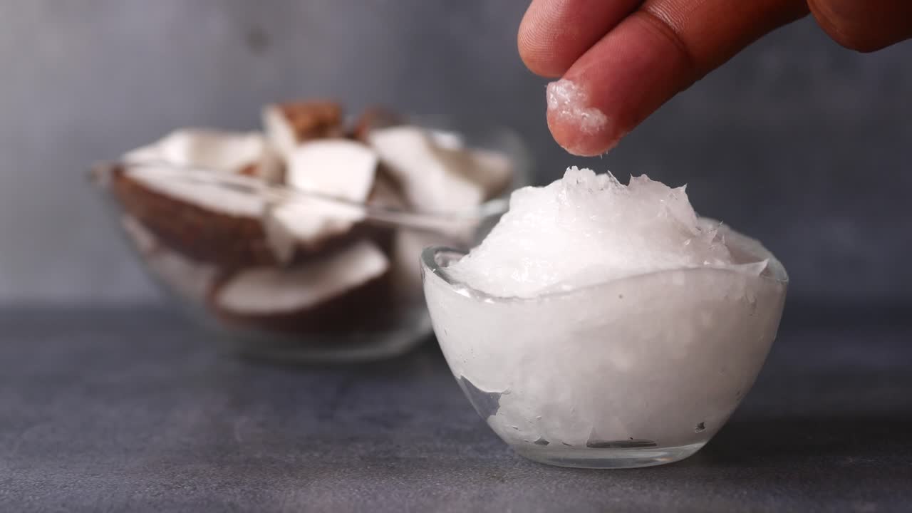 aceite de coco en un cuenco con pedazos de coco al fondo