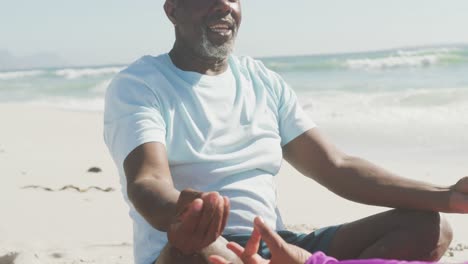 Senior-african-american-couple-practicing-yoga-and-meditating-on-sunny-beach