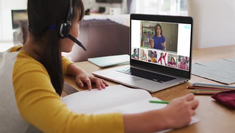 Schoolgirl-using-laptop-for-online-lesson-at-home,-with-diverse-teacher-and-class-on-screen