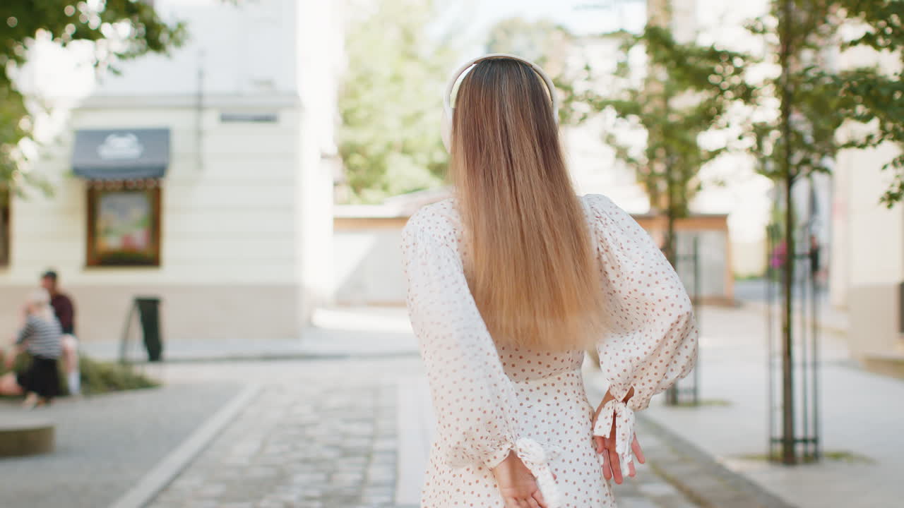 무선 헤드폰을 착용한 행복한 백인 여성이 도시 거리에서 음악을 듣고 춤을 추는 모습