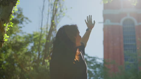 woman raising hand in a park near a building