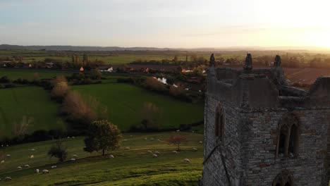 Antena-Hacia-Atrás-Revela-Una-Toma-De-La-Iglesia-De-Las-Paperas-De-Madriguera-Con-El-Resplandor-De-Una-Puesta-De-Sol-Sobre-Los-Niveles-De-Somerset