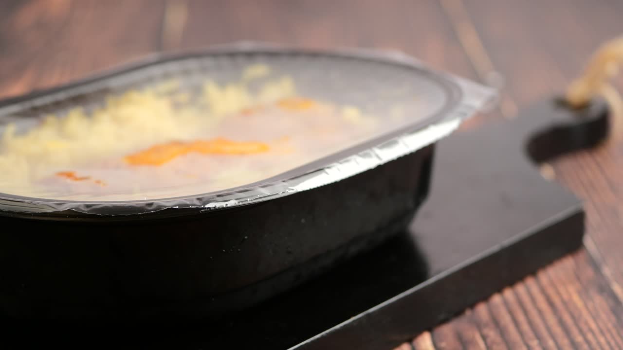 Pre-packaged frozen meal in a container on a wooden surface