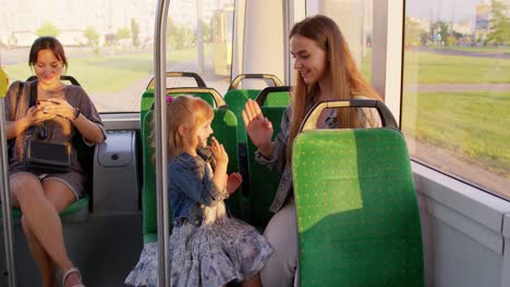 family rides in public transport tram, mother with girl sit together and playing game clapping hands