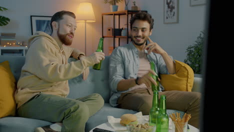 two men watching tv and enjoying drinks at home