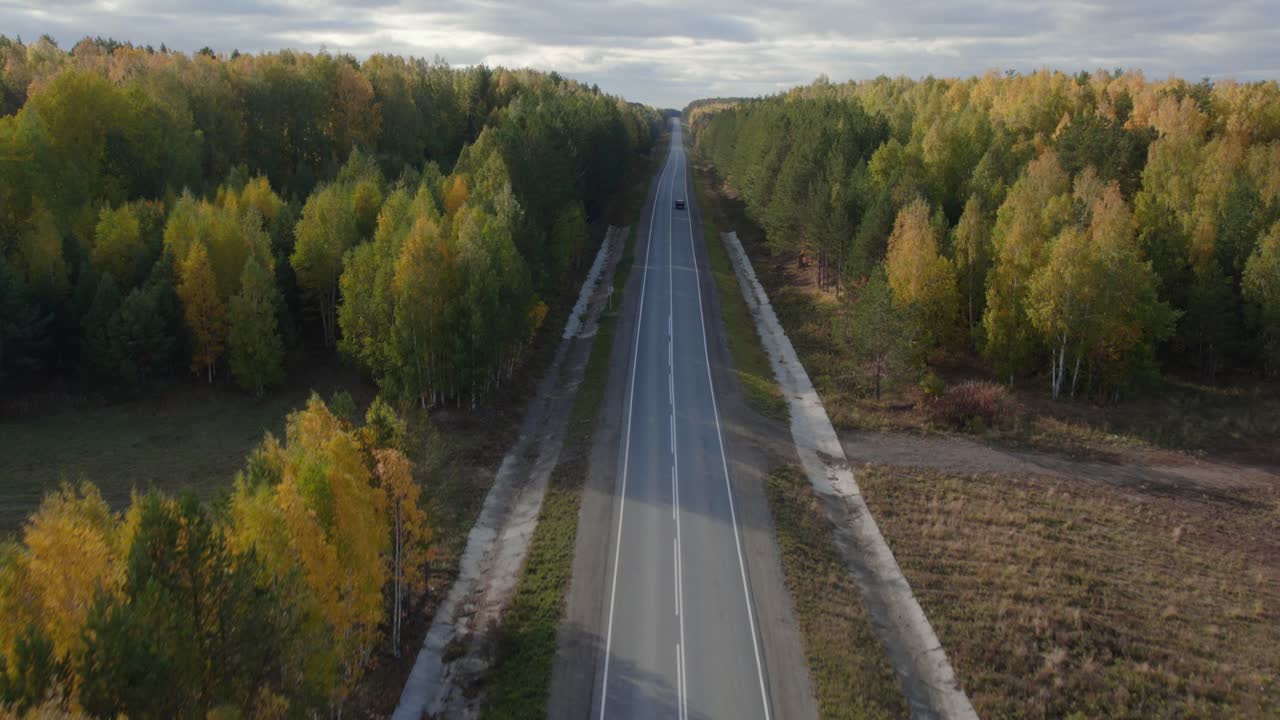 Съемка с дрона длинного прямого асфальтового шоссе, пролегающего через красочный осенний лес, с одной машиной, едущей вдалеке, Уральский регион, Россия.
