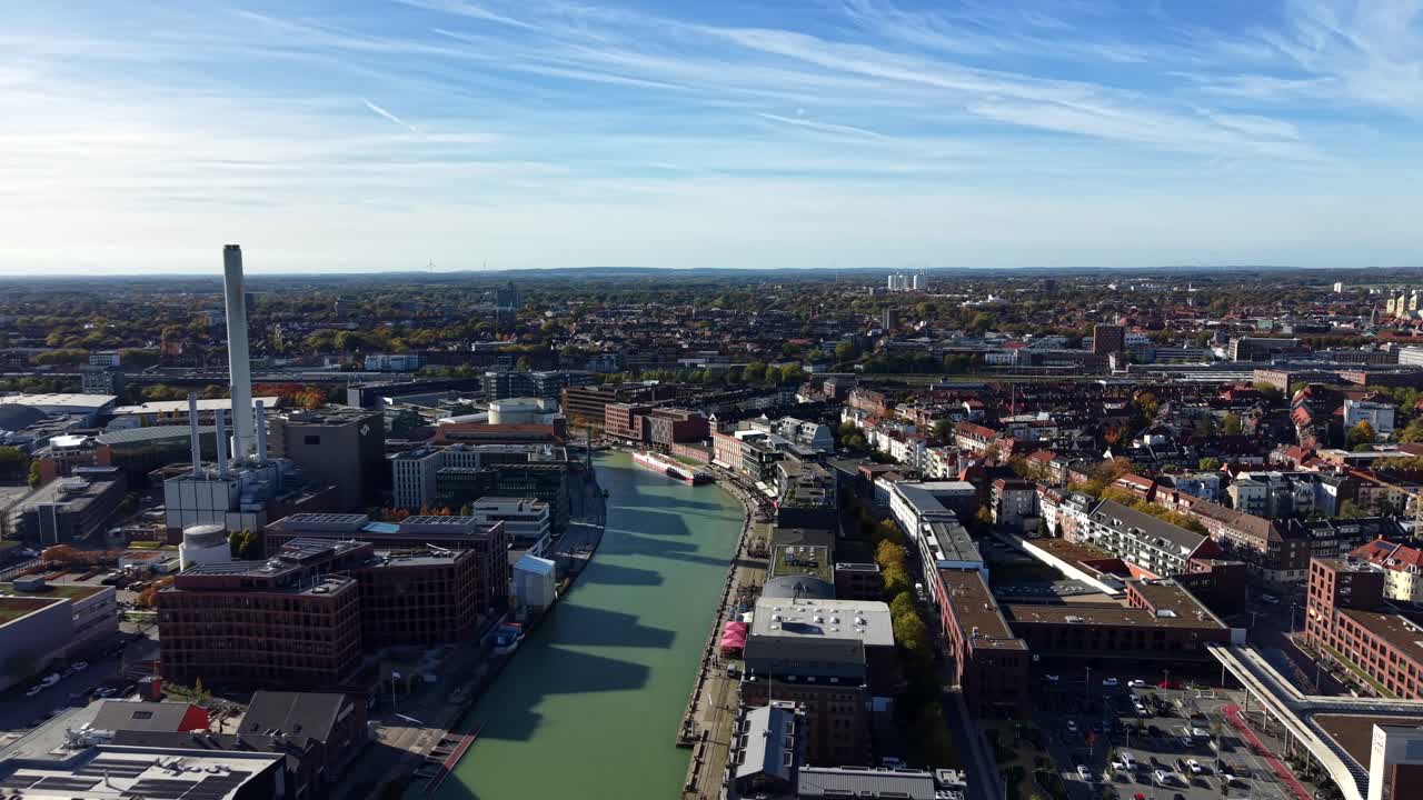 River flowing through German city of Münster during sunny day. Modern buildings and houses in German town. Blue sky and colored trees in autumn season. Wide shot. Drone flight
