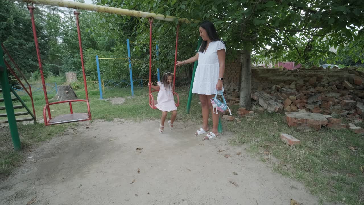 una madre embarazada y su hija joven disfrutan de un tiempo de juego juntos en un patio de recreo en el parque, rodeados de árboles y vegetación