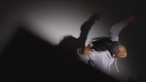 looking down on studio shot of young woman dancer wearing hoodie dancing in spotlight in slow motion 1