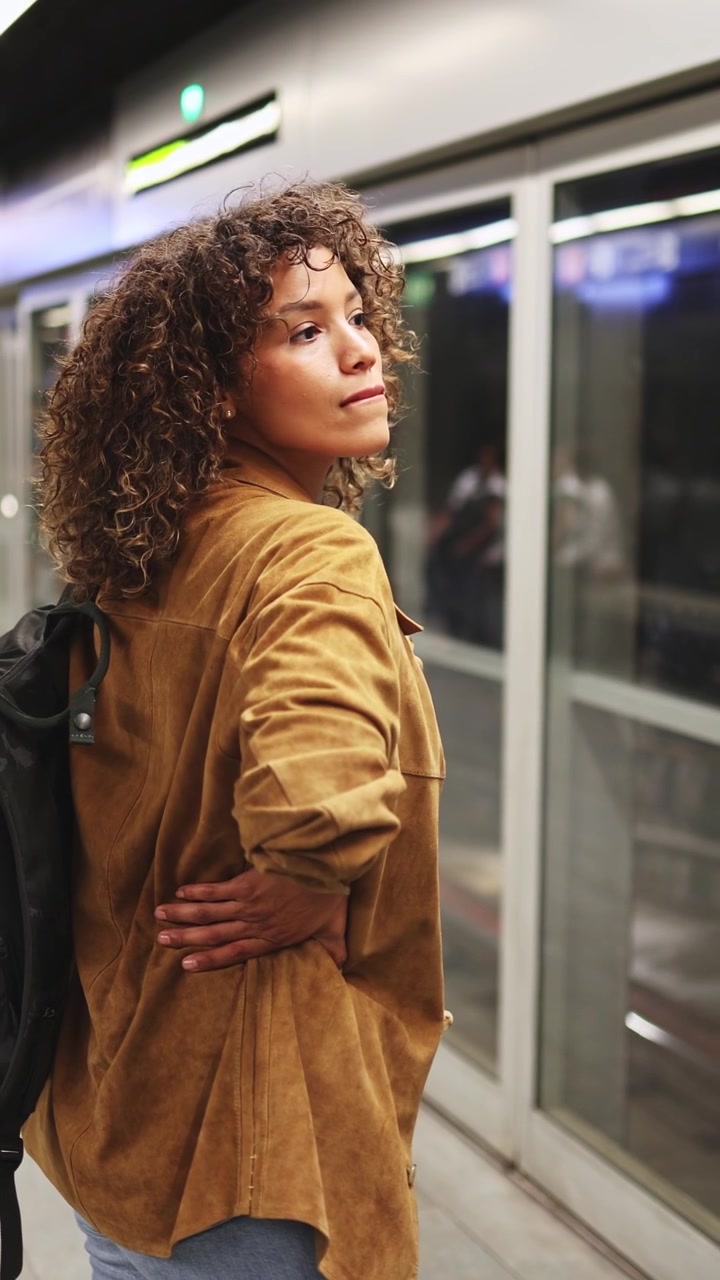 Mujer con cabello rizado y mochila esperando en el andén del metro
