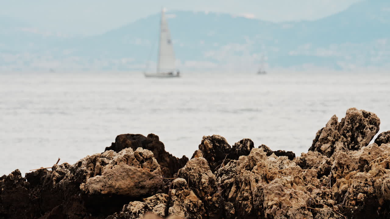 Close up of rugged rocks on the shore with a blurred view of a boat moving on the sea in the background