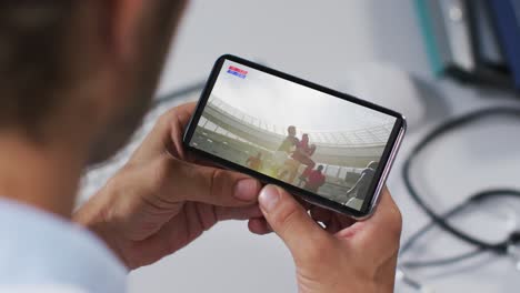 Compuesto-De-Un-Médico-Masculino-Viendo-Un-Partido-De-Rugby-En-Un-Teléfono-Inteligente