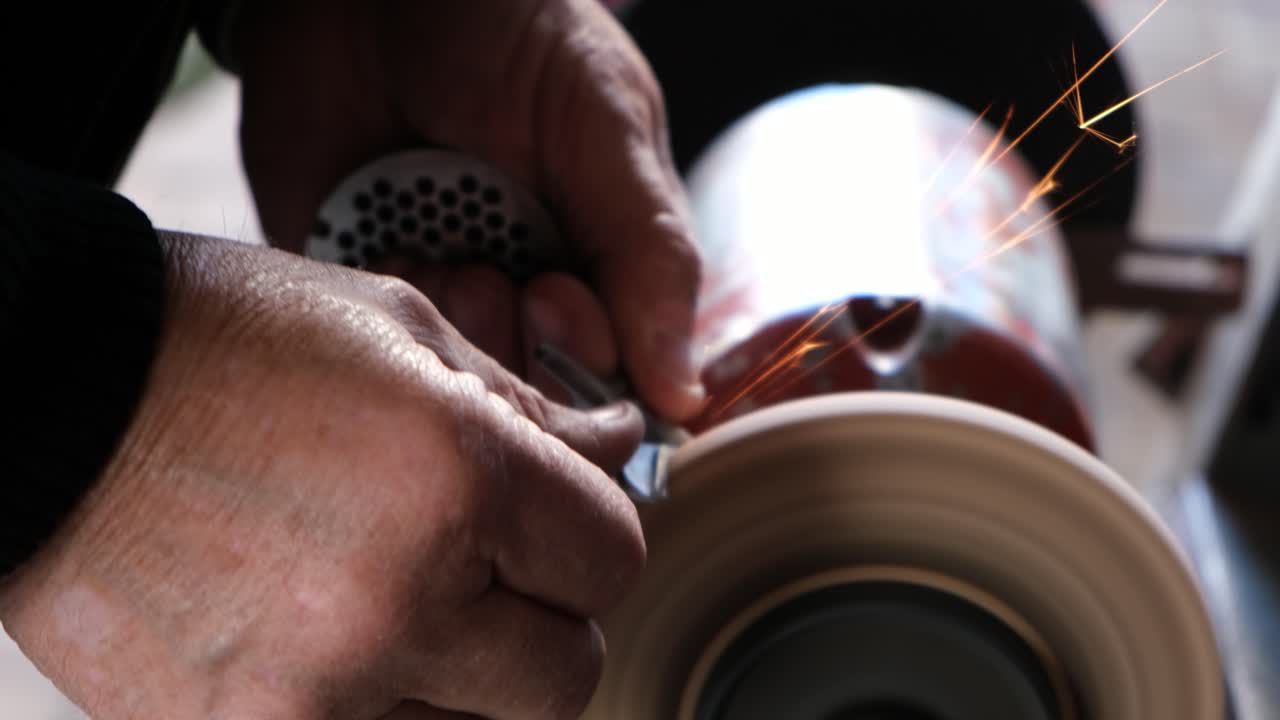 Close up shot of an old man's hands sharpening a metal object using a grinding wheel