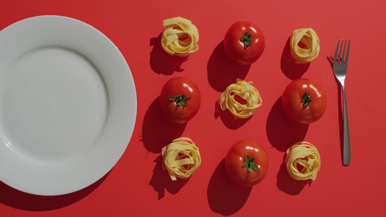 video de tomates rojos frescos y nidos de pasta con plato y tenedor en fondo rojo
