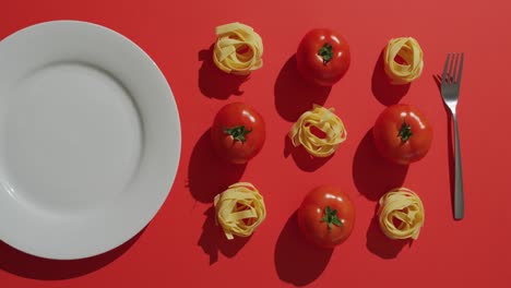 video of fresh red tomatoes and pasta nests with plate and fork on red background