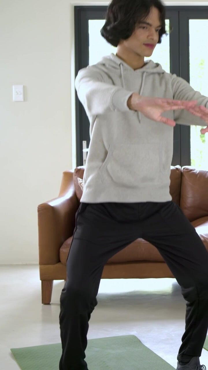 Vertical video: Receiving hand, man in gray hoodie doing squats on mat at home ring light recording