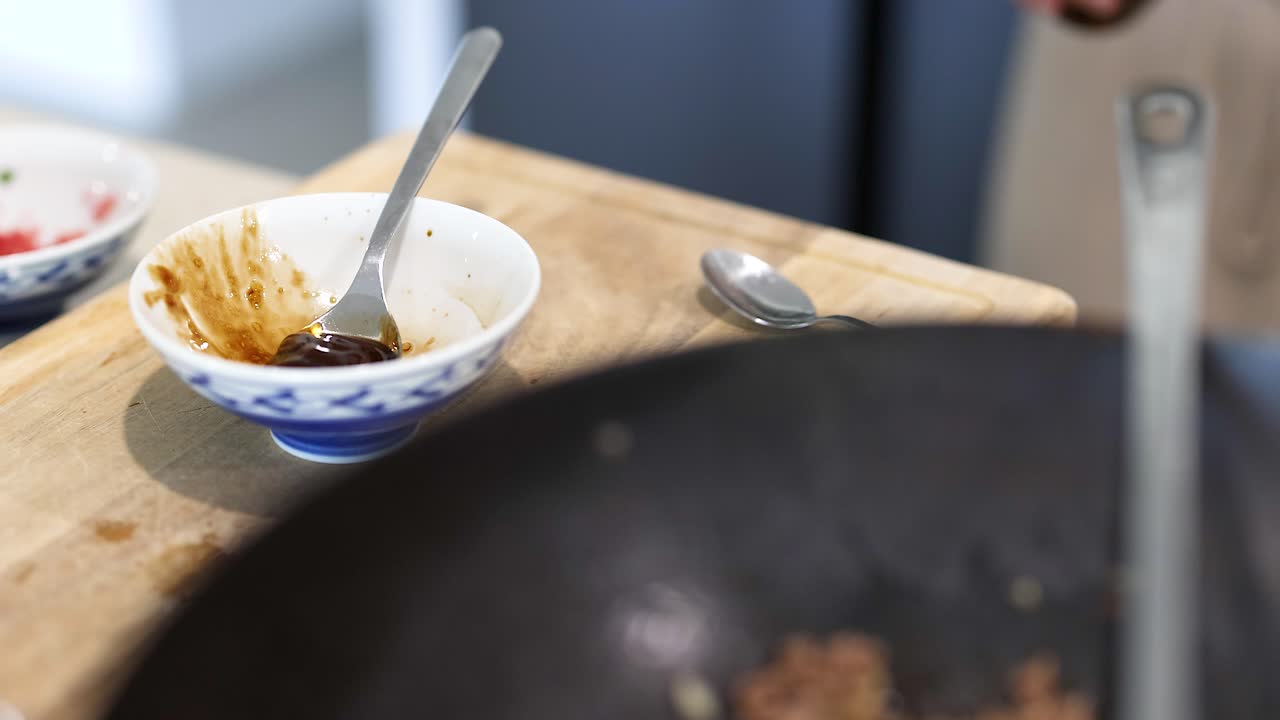 A person prepares sauce in a bright kitchen, focusing on a bowl with a spoon. Natural lighting enhances the scene