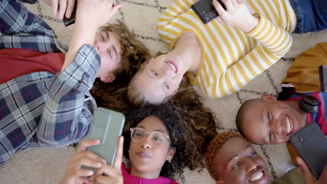 happy diverse group of teenage friends using smartphones and lying on carpet at home, slow motion