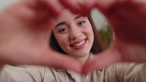 Una-Joven-Feliz-Hace-Un-Símbolo-De-Amor-Mostrando-Un-Signo-De-Corazón-A-La-Cámara-Expresa-Sentimientos-Románticos