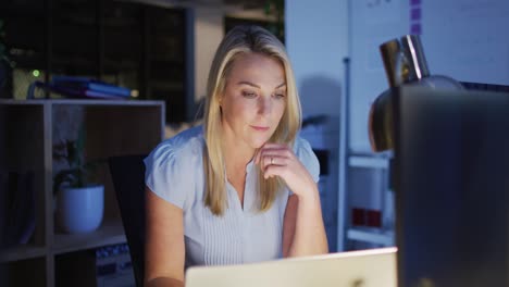 Video-of-focused-caucasian-woman-using-laptop,-working-late-in-office