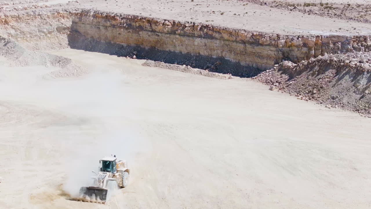 Aerial view of a bulldozer dusting and lifting gravel at a sand pit, sunny day