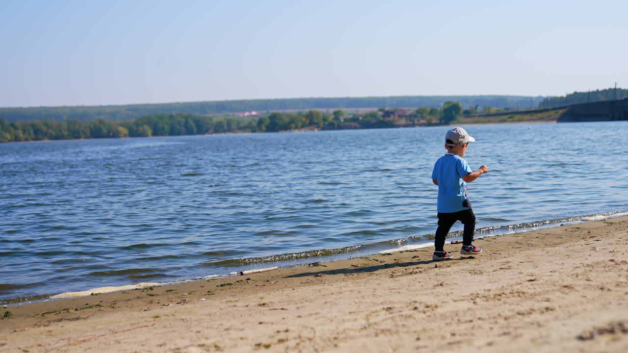 Little boy walking by the sandy shore. Toddler kid spending time on the river bank on sunny weather.