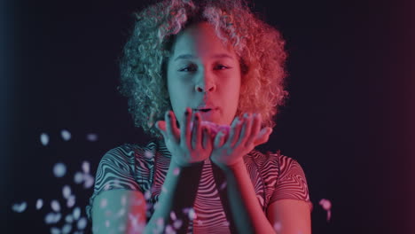Woman with curly hair blowing confetti in neon lights