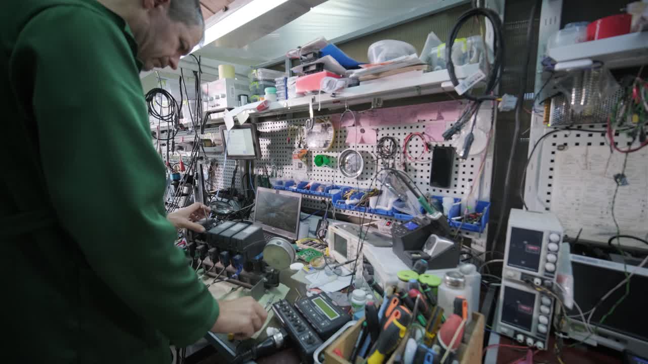 tienda de reparación de equipos electrónicos. el técnico ingeniero soldada la placa de circuitos impresos de un dispositivo electrónico bajo un microscopio.