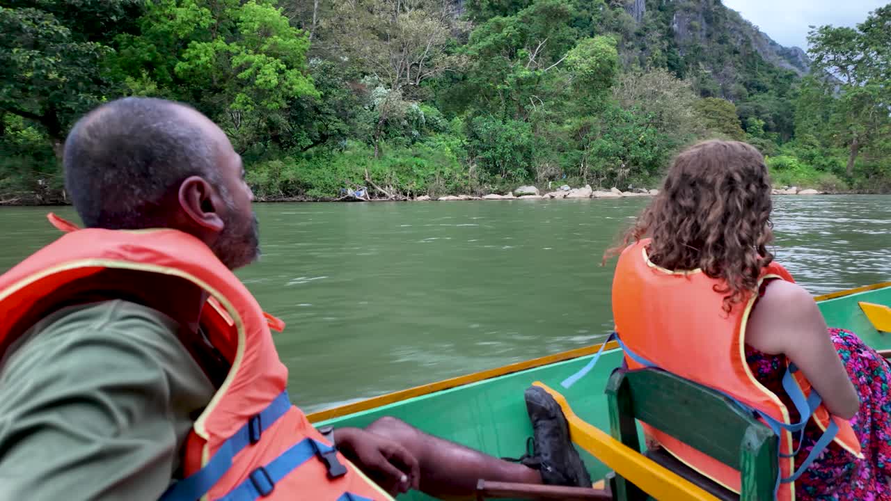 Couple wearing life vests enjoying a river boat trip through the scenic landscape of Laos