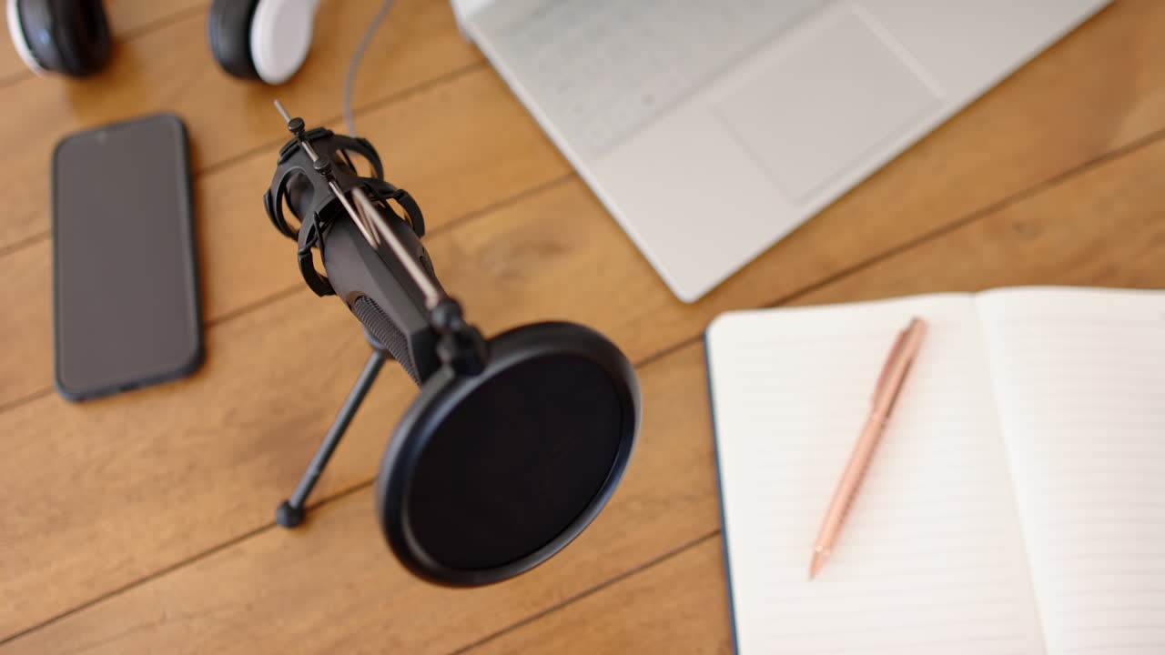 Podcasting setup with microphone, laptop, smartphone, and notepad on wooden table, at home