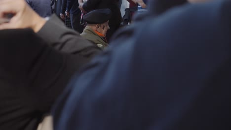 an elderly veteran, dressed in military attire, sits in a wheelchair during a solemn military commemoration. his quiet reflection embodies the honor and respect for his service