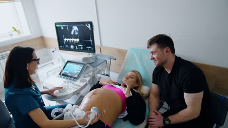 pregnant woman talks to the doctor during ultrasound examination. smiling man sits beside listening. top view.