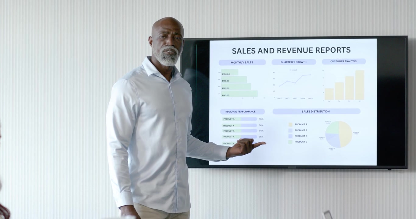 Diverse team in meeting seeing senior African American man walking to monitor showing sales charts