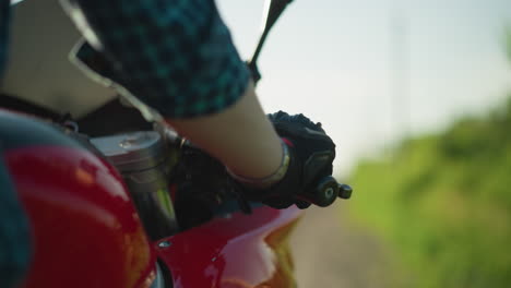 close-up of a biker starting her bike as her shirt flutters in the wind, the background is blurred with greenery