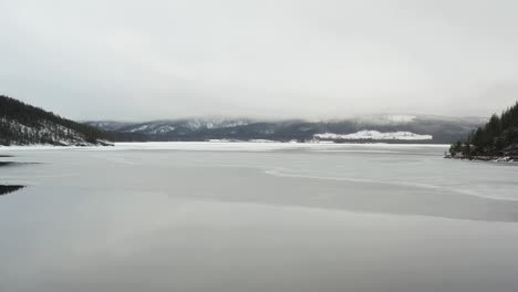 aerial shot of a partially frozen lake or reservoir in the middle of sweden during the midwinter solstice. low angle shot towards the frozen lake.