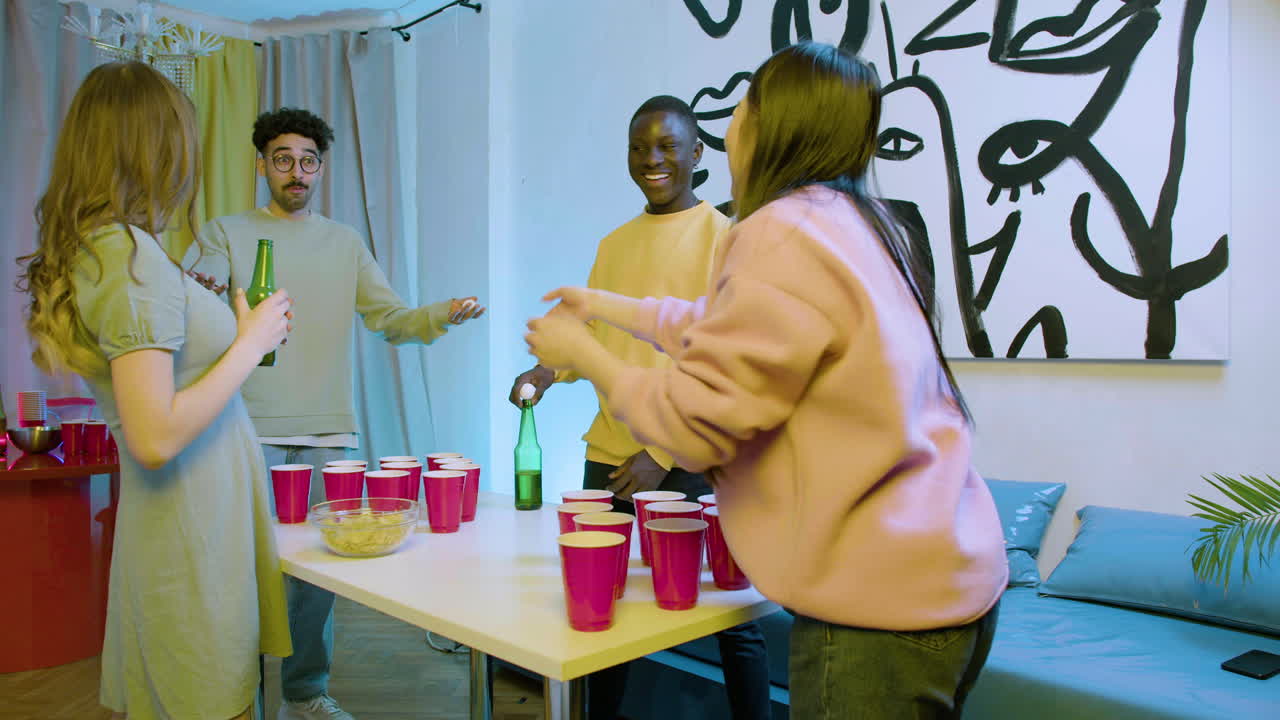 Happy multiethnic young friends playing beer pong at home
