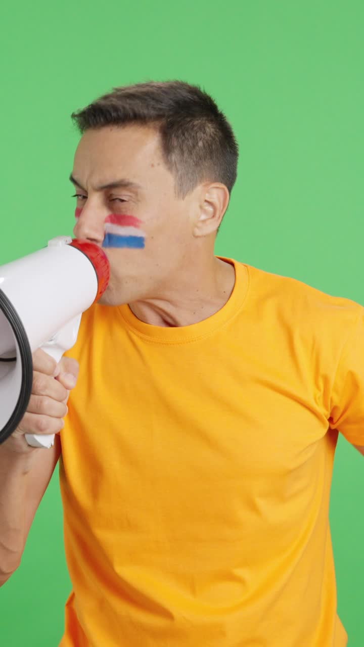 Uomo entusiasta con la bandiera olandese dipinta sul volto che usa un megafono