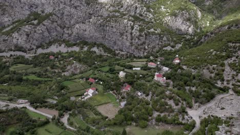 descriptive panning drone video advancing on the sh20 highway in albania, over a village in a valley at the height of javor and mreg, cloudy sky, houses in the village and farmland