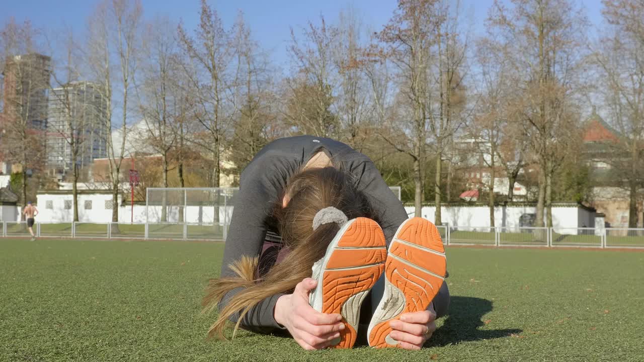 Fit young flexible woman stretching out lower back in park
