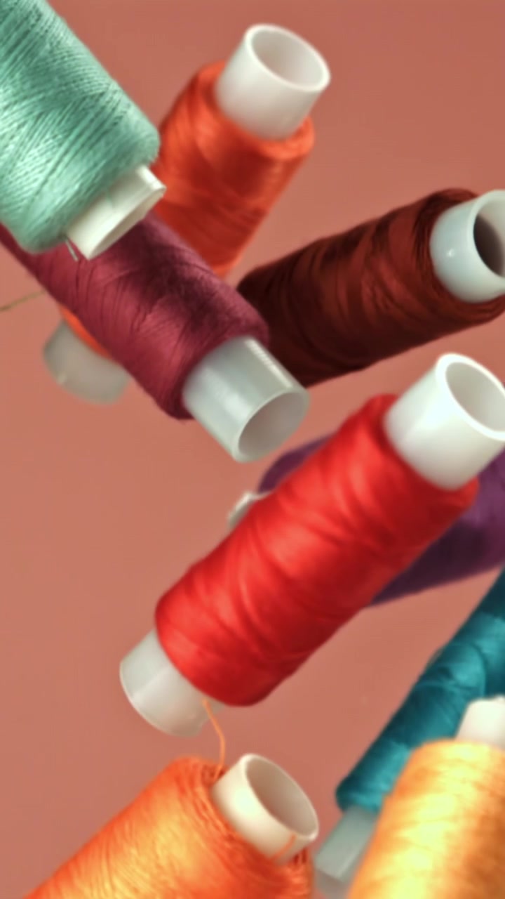 Colorful Thread Spools Falling and Rising Against a Solid Background